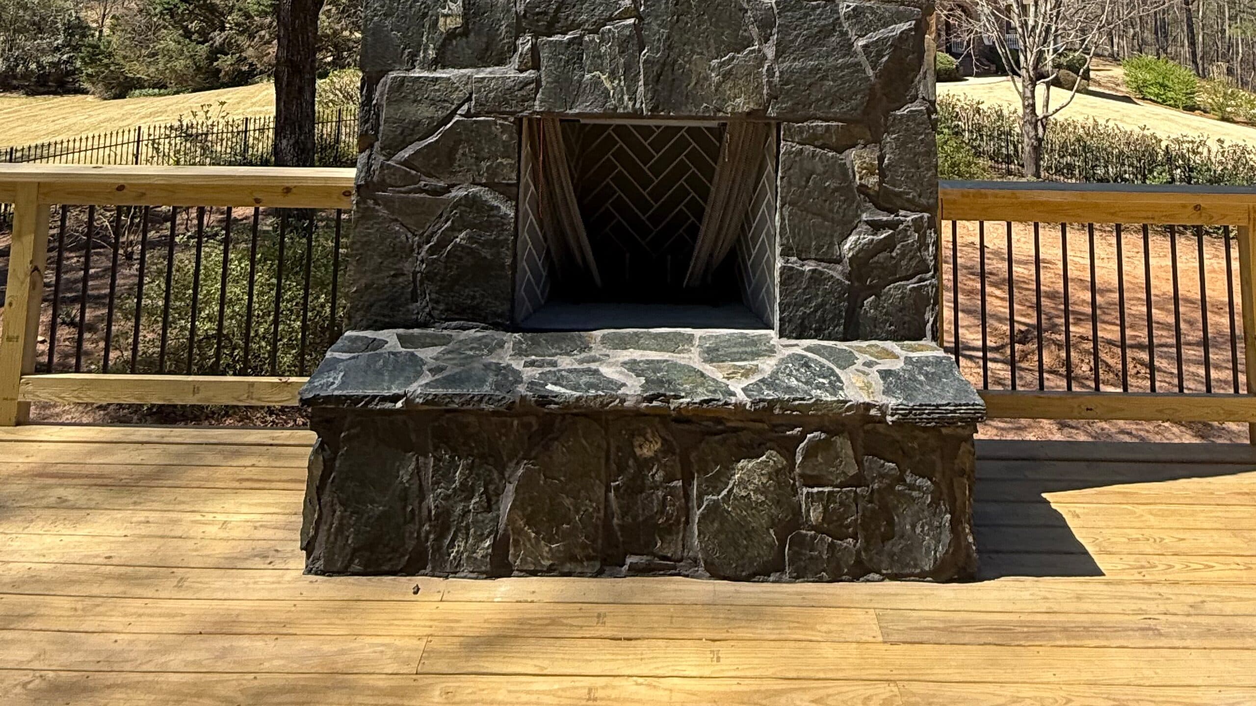 Finished outdoor stone fireplace with a herringbone firebox on a wood deck